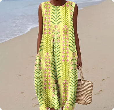 Woman in a yellow patterned dress standing on a beach.