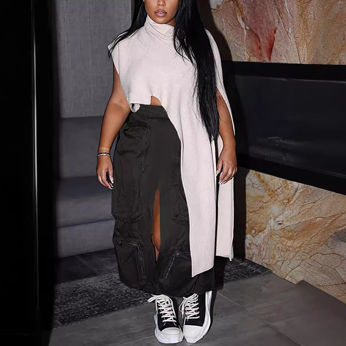 Person wearing a long beige cardigan over black pants with white sneakers in an indoor setting.