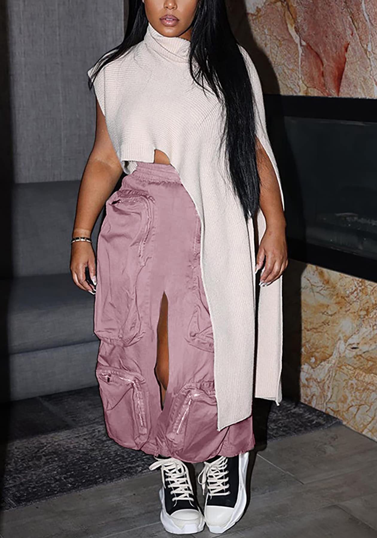 Person wearing a long beige coat over a white top and pink cargo pants, standing indoors.