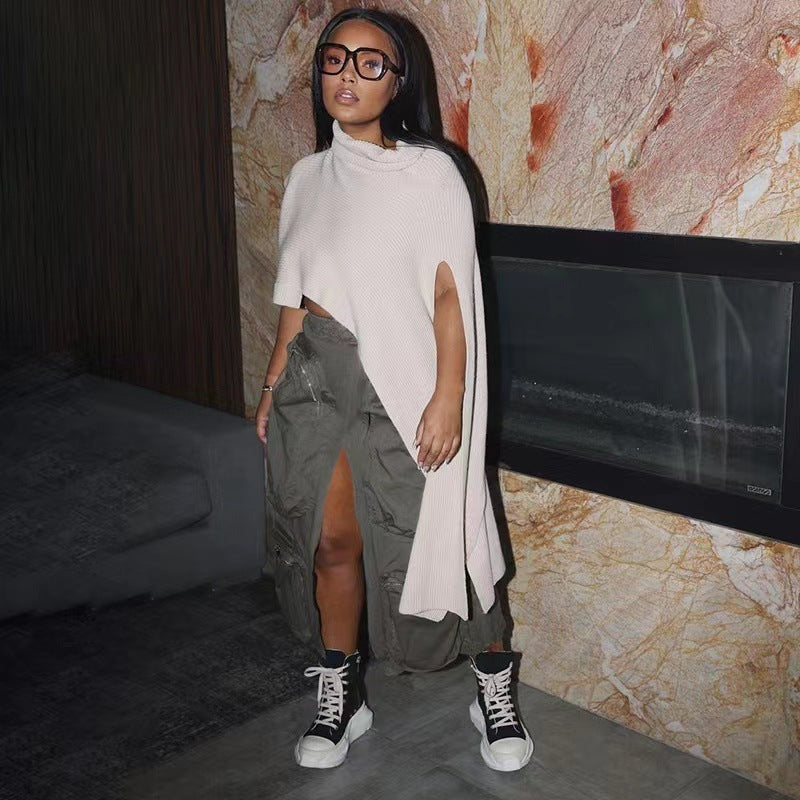Woman wearing a white top and green cargo pants with black sneakers in a room with a stone wall.