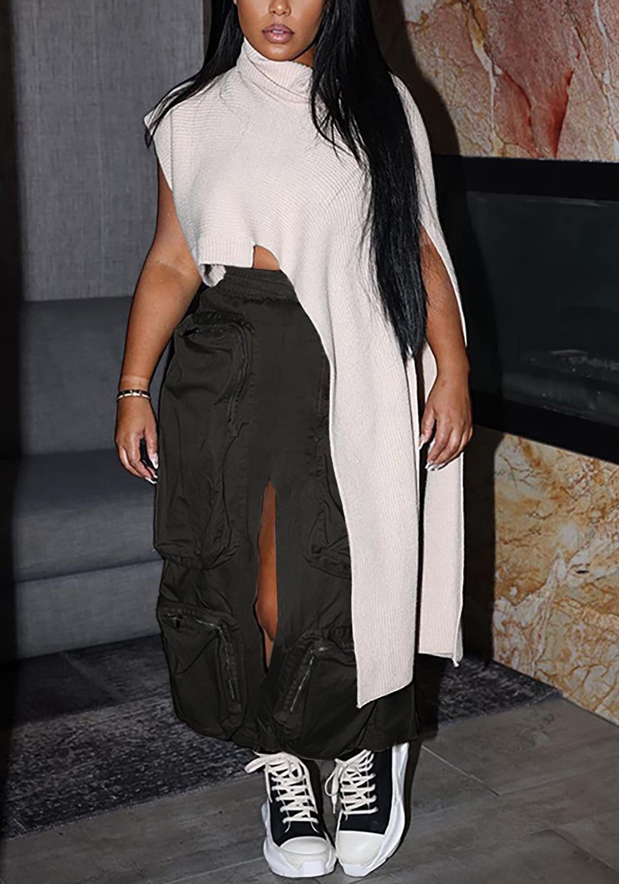 Female model wearing a long beige cardigan over a black outfit with white sneakers in an indoor setting.