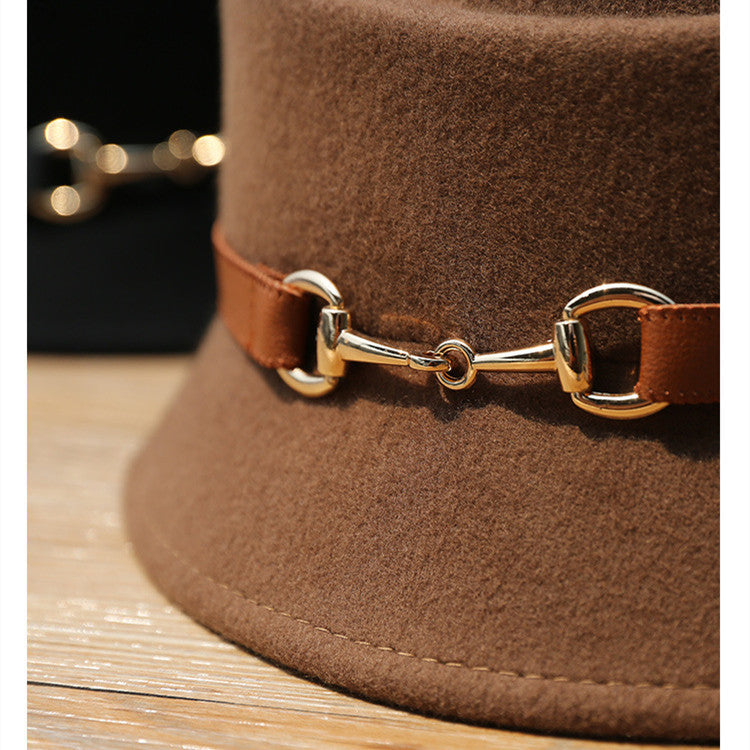Brown hat with a gold and leather bridle detail on a wooden surface