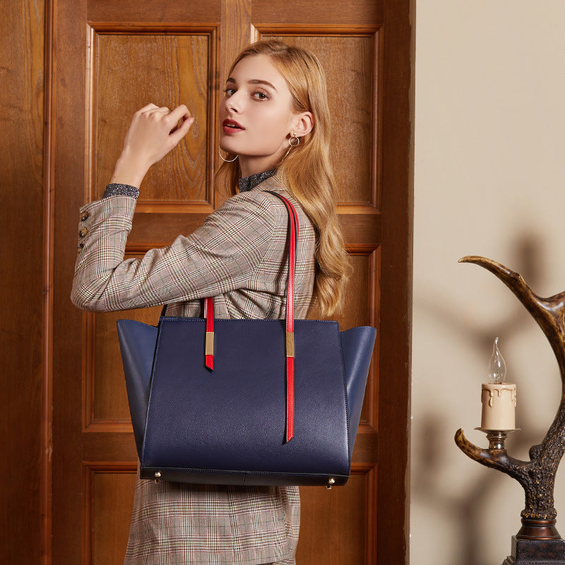Woman holding a blue handbag with red accents in a warm-toned interior setting