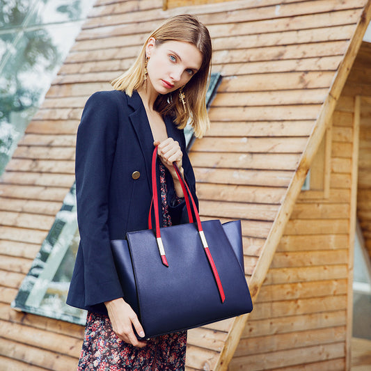 Woman holding a navy blue handbag with red straps in front of a wooden structure