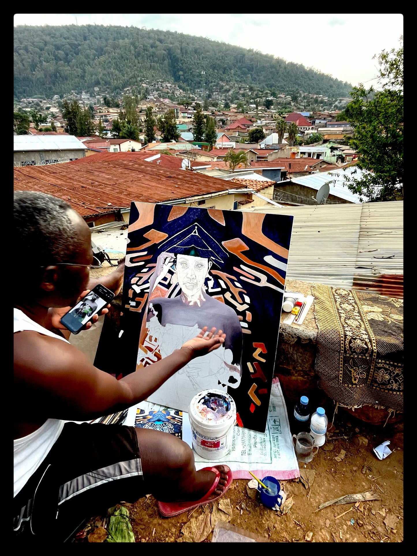 Ugandan painter G Brain paints a portrait of a succubus on raffia background while overlooking rwandan landscape